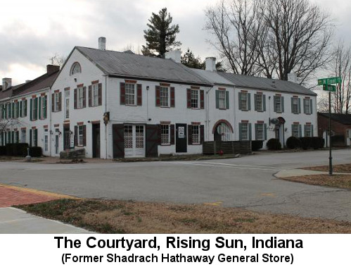 Color photo: Large, whitewashed 2-story stucco building with red shutters.